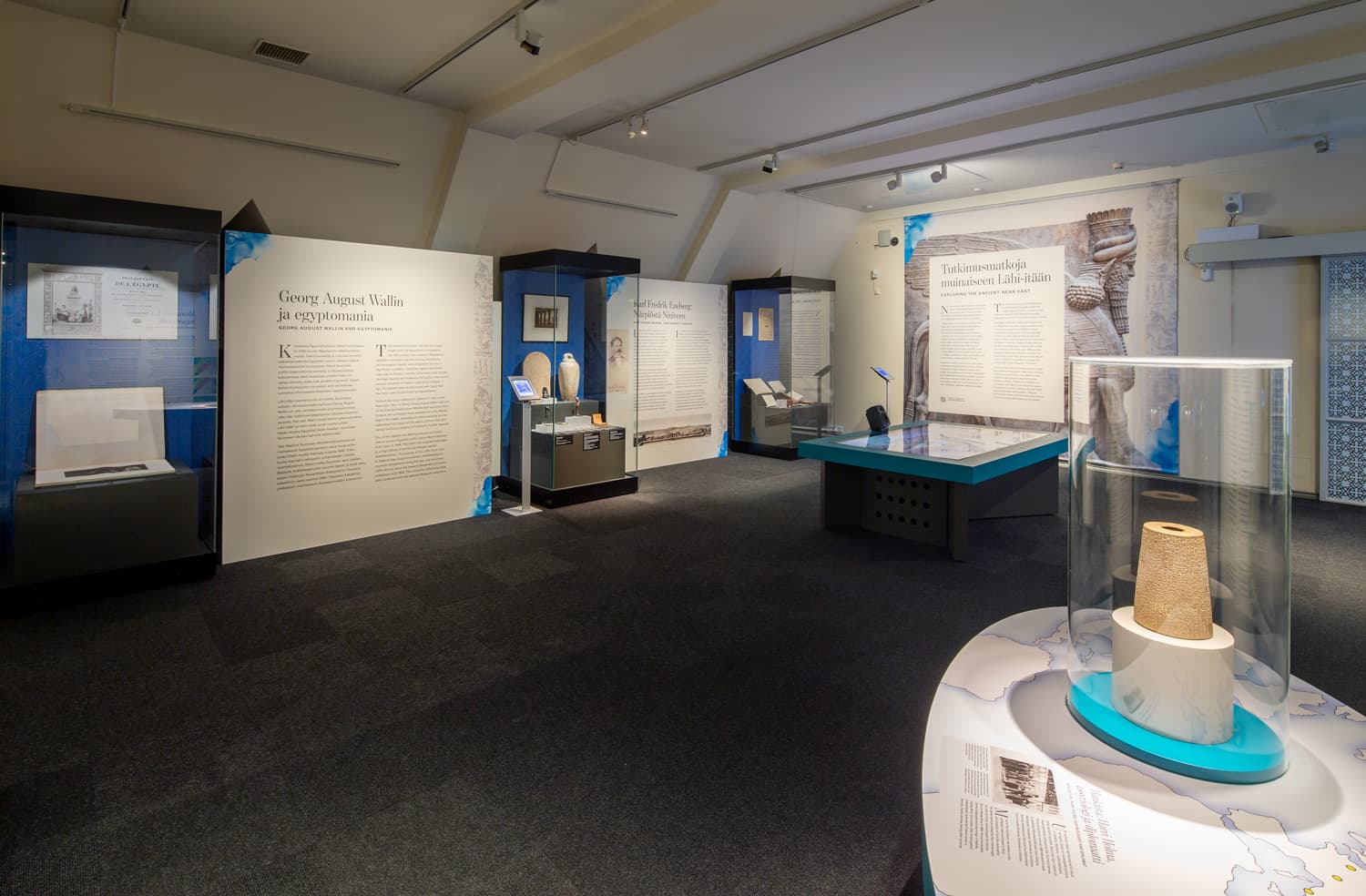 Kuva on Kansallismuseon Lähi-itä näyttelystä. Kuvassa näkyy näyttelyn esineitä ja tekstitauluja.